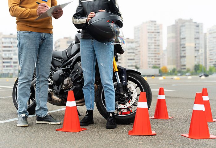 Alumna con su casco junto a una moto y un instructor tomando notas en un circuito con conos